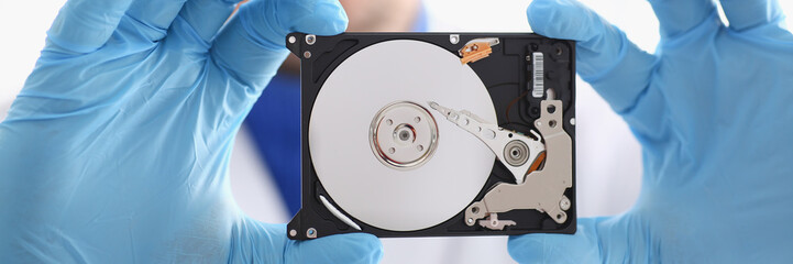 A male repairman wearing blue gloves is holding a hard drive from computer or laptop in hands....
