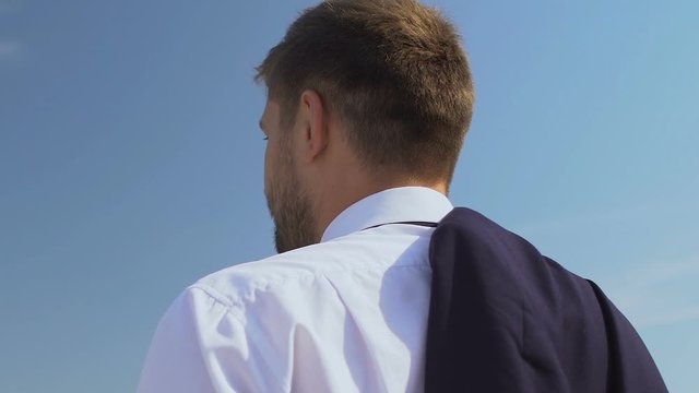 Inspired male boss putting jacket on shoulder and enjoying skyscape, back view