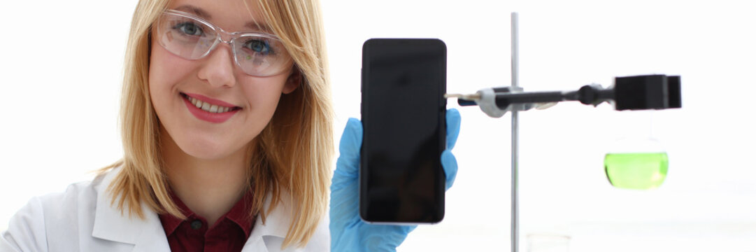 A female doctor in a chemical laboratory holds a smartphone in his hand with display, you can insert a picture or an image you want to write for an advertising company