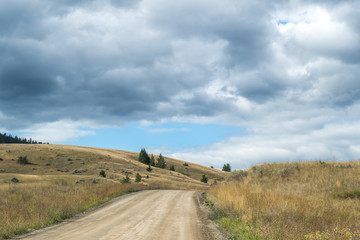 Winding dirt road in the rural British Columbia near Kamloops. dry grassland, bush and shrub, occasional conifers trees, hills, desert like landscape. Road less traveled