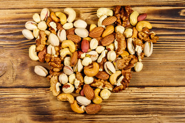 Pile of mixed nuts in shape of heart on wooden table. Top view. Walnuts, pistachio, almond, peanut, cashew, hazelnut on wood background. Healthy eating concept