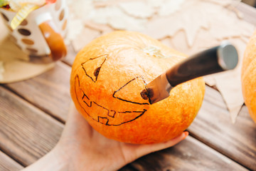 Female hand holding pumpkin with drawing Jack-o-lantern sketch and knife.
