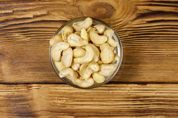 Glass bowl with raw cashew nuts on a wooden table. Top view