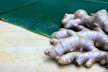 Fresh ginger root and ginger sliced on green leaf background on wood table background, healthy Asian herb concept