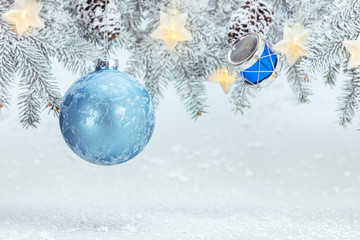 Fototapeta na wymiar snowy christmas tree branches decorated with blue glass ball, drum toy and star garland lights