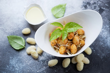Bowl of potato gnocchi with red pesto sauce, parmesan and green basil over grey stone background, elevated view
