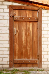 Old dirty shabby wooden door covered in brown paint. With a handle and constipation inserted into a wall of white silicate brick.