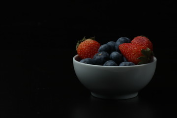 a bowl of strawberry and blueberry isolated on black background