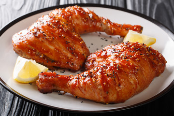 Closeup baked sticky chicken legs quarters served with lemon on a plate. horizontal