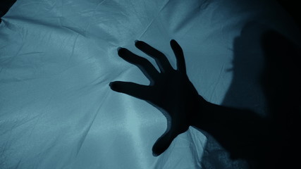 Creepy night scene: A woman's silhouette behind the fabric, a hand suddenly hits the fabric,...