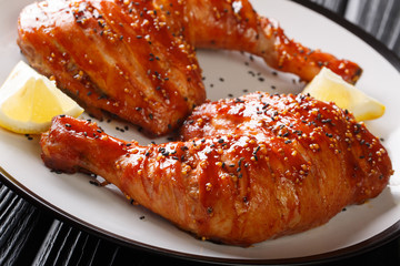 Traditional glazed sticky chicken leg quarters served with lemon closeup on a plate on the table. horizontal
