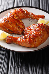 portion of sticky chicken quarter legs with sesame seeds and lemon close-up. vertical