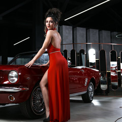 Sexy girl in a red dress posing on a background of red cars