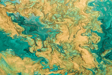 Acrylic fluid art. Abstract golden waves on green background with golden inclusions. Free flowing paint