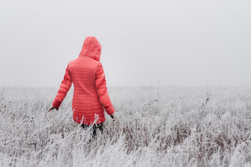 Woman in red coat walking in frosty field on foggy day