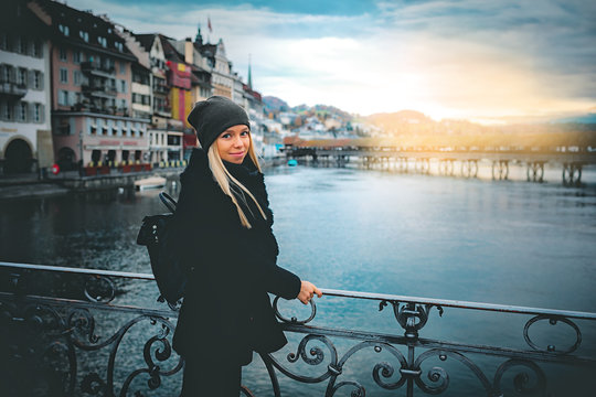 Young beautiful pretty blonde tourist girl in warm hat and coat with backpack walking at cold autumn in Europe city enjoying her travel in Zurich Switzerland