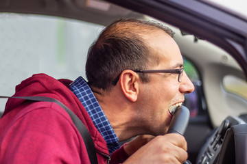 Angry driver bites the steering wheel. Traffic jams concept.