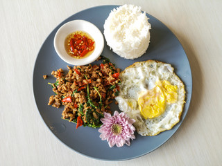 Fototapeta na wymiar Spicy Thai food rice topped stir-fried pork and basil with Fried egg in gray dish on wooden table.