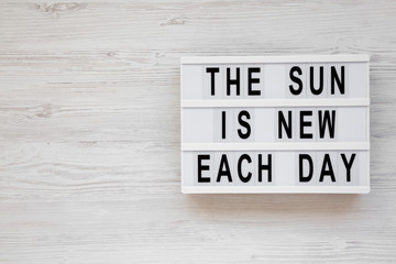 'The sun is new each day' words on a lightbox on a white wooden background, top view. Overhead, from above, flat lay. Copy space.