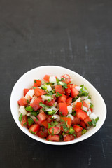 Pico de Gallo in a white bowl on a black background, low angle view. Copy space.