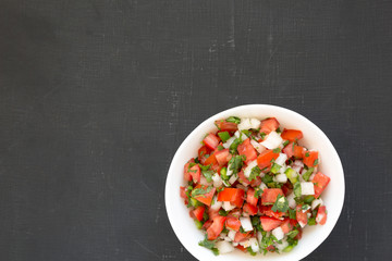 Pico de Gallo in a white bowl on a black background, top view. Overhead, from above, flat lay. Copy space.