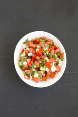 Pico de Gallo in a white bowl on a black background, overhead view. Top view, from above, flat lay.