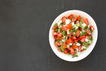 Top view, Pico de Gallo in a white bowl on a black surface. Overhead, from above, flat lay. Space for text.