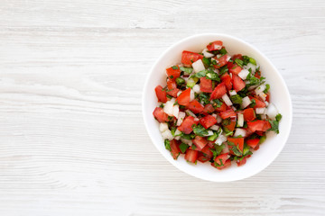 Pico de Gallo in a white bowl on a white wooden surface, top view. Overhead, from above, flat lay. Space for text.