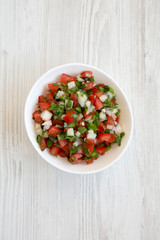 Pico de Gallo in a white bowl on a white wooden surface, top view. Overhead, from above, flat lay.