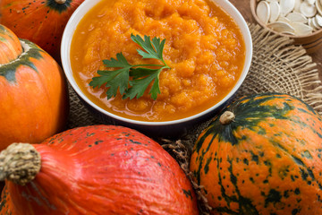 Pumpkin porridge in a bowl among orange pumpkins. Close-up