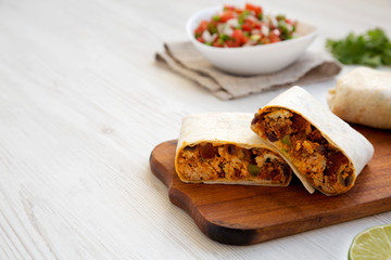 Homemade chorizo breakfast burritos on a rustic wooden board on a white wooden surface, side view. Copy space.