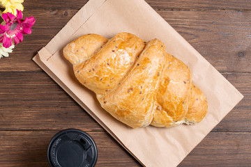 croissant in paper bag on wooden background with paper disposable cup of coffee. concept of continental breakfast and eco packaging