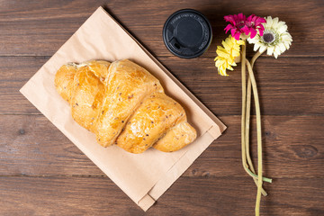 croissant in paper bag on wooden background with paper disposable cup of coffee. concept of continental breakfast and eco packaging