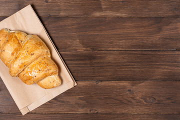 croissant in paper bag on wooden background. concept of continental breakfast and eco packaging, recycling of raw materials and place for copy space