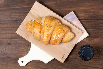 croissant in paper bag on wooden background with paper disposable cup of coffee. concept of continental breakfast and eco packaging