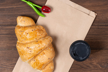 croissant in paper bag on wooden background with paper disposable cup of coffee. concept of continental breakfast and eco packaging