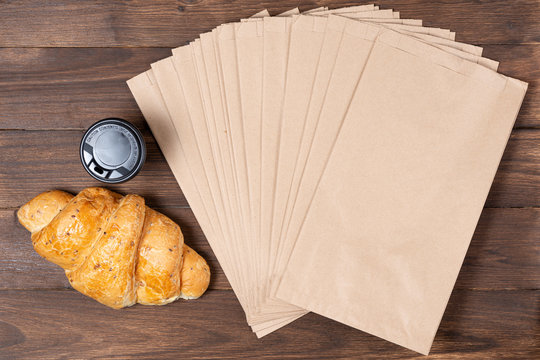 croissant in paper bag on wooden background with paper disposable cup of coffee. concept of continental breakfast and eco packaging