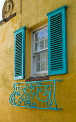 Fototapeta na wymiar Colorful yellow wall and window with blue shutters and balconet.