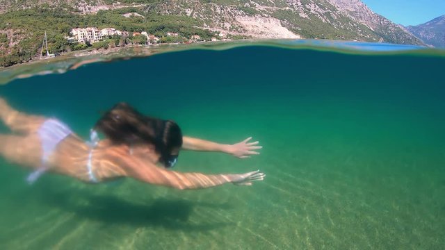 Slowmotion. Woman snorkeling at the sea. Half view of ocean and mountains.