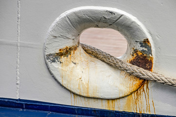 Grey rope trough a somewhat rusty opening in the white hull of a ship
