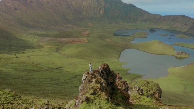 Woman on the edge of rock above huge caldera of inactive stratovocano. Aerial of Caldeirao, Corvo, Azores