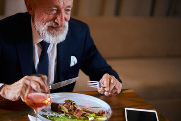 Mature beared businessman in tidy beautiful suit eat and drink champagne in romantic atmosphere. Light smoke from the fireplace on the side. Restaurant, cafe concept