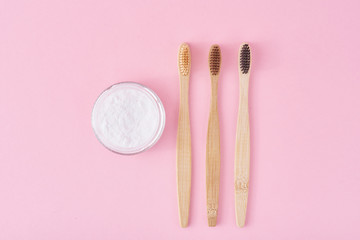 Three wooden bamboo toothbrushes and baking soda powder in glass jar on a pink background.  Teeth health and keep mouth concept