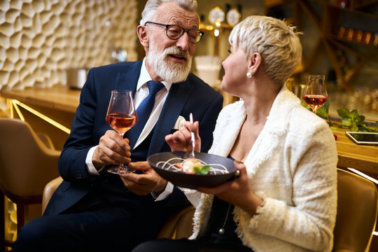 Caucasian man in suit and eyeglasses, beautiful woman in white elegant blazer enjoy meal in attractive place. Sweet dessert and glass of champagne. Love in the air