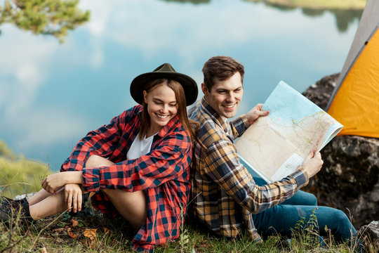 handsome positive man and beautiful woman in stylish checked shirts sitting back to back, having fun outdoors. close up side view photo, free time spare time