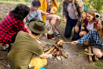 young tourists gathering around the bonfira and roasting mushrooms, close up photo