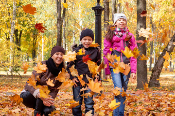 Fototapeta na wymiar happy family playing with fallen leaves in autumn park