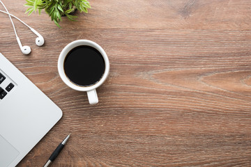 Wood office desk table with laptop computer, cup of coffee, pen, earphones and plant pot. Top view with copy space, flat lay.