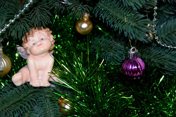 A little angel sits on a green branch of a Christmas tree, the Christmas tree is dressed up, the New Year is coming.