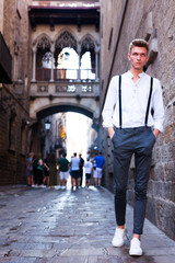 Fototapeta na wymiar young European guy in shirt and trousers with suspenders walking around city
